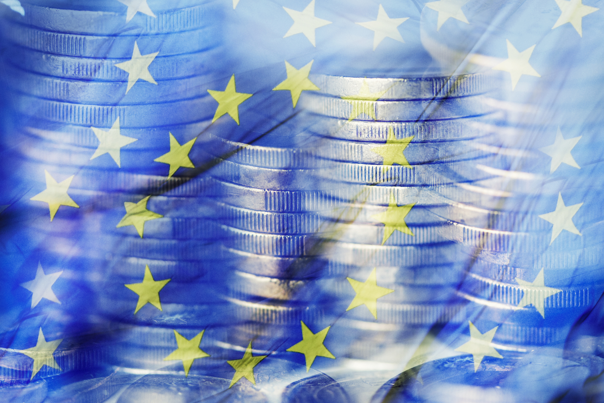 Imatge difuminada amb monedes apilades i la bandera de la Comunitat Europea