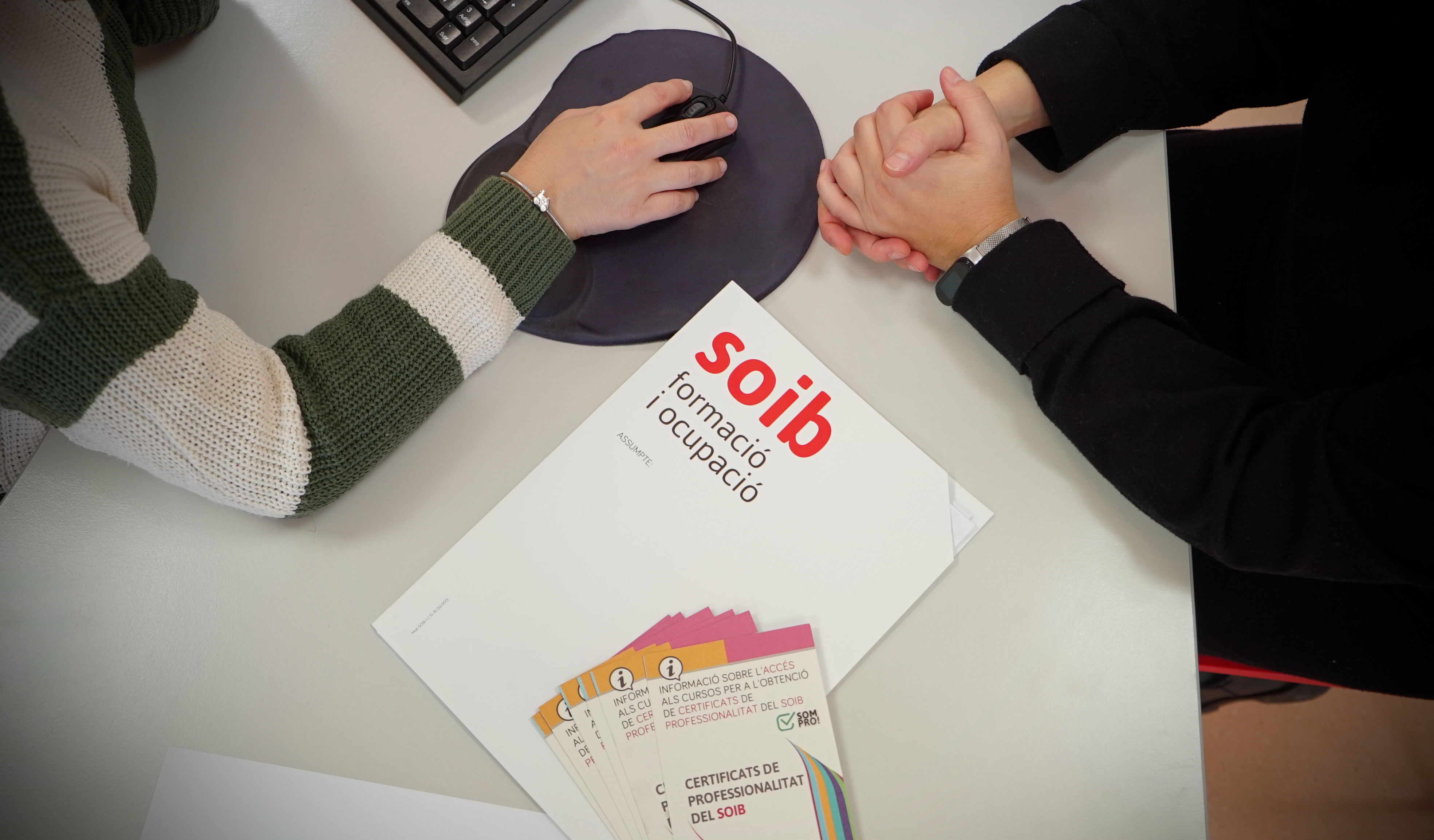 Manos sobre ratón de ordenador y libro con el logotipo del SOIB