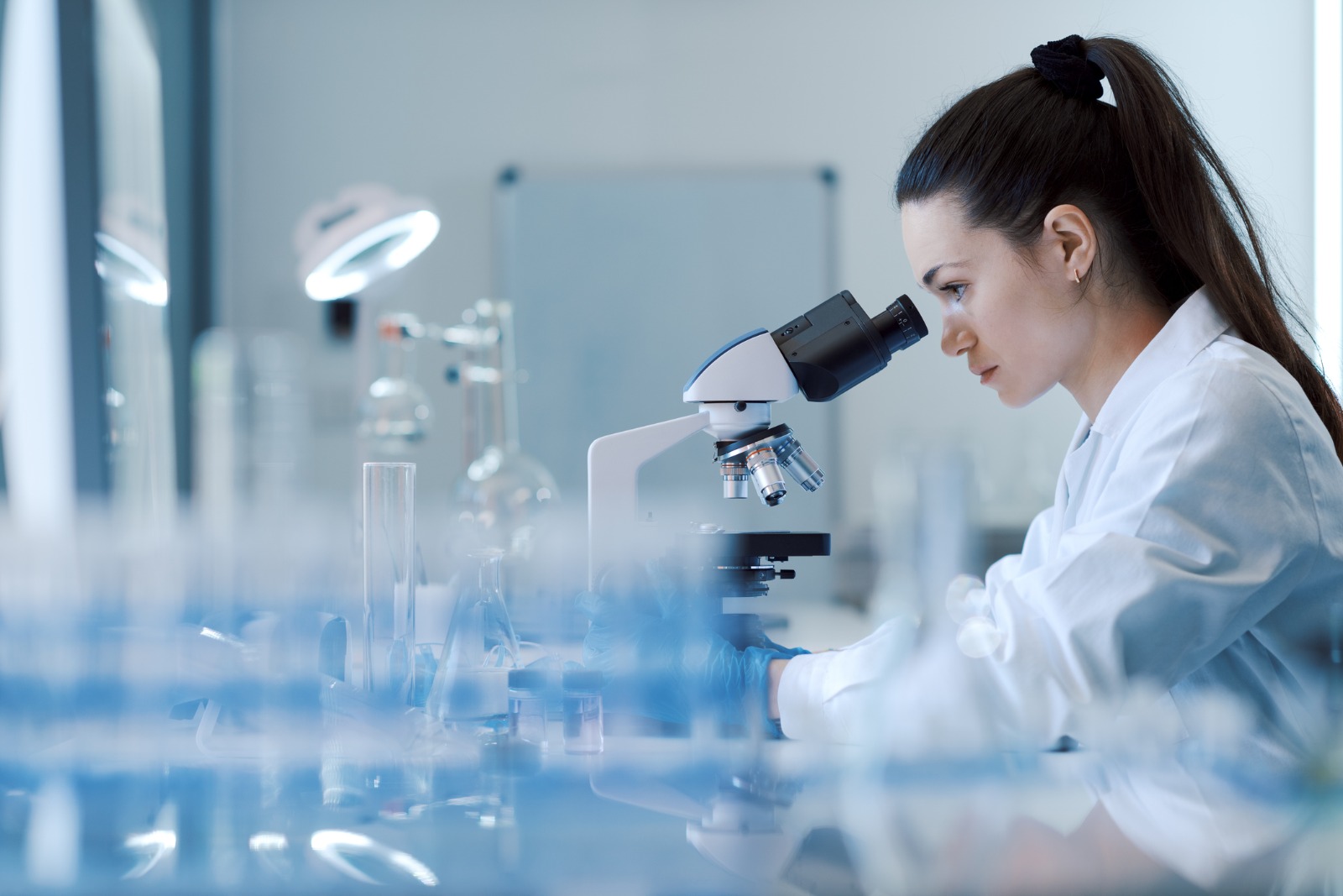 Una investigadora mira a través d'un microscopi a un laboratori.