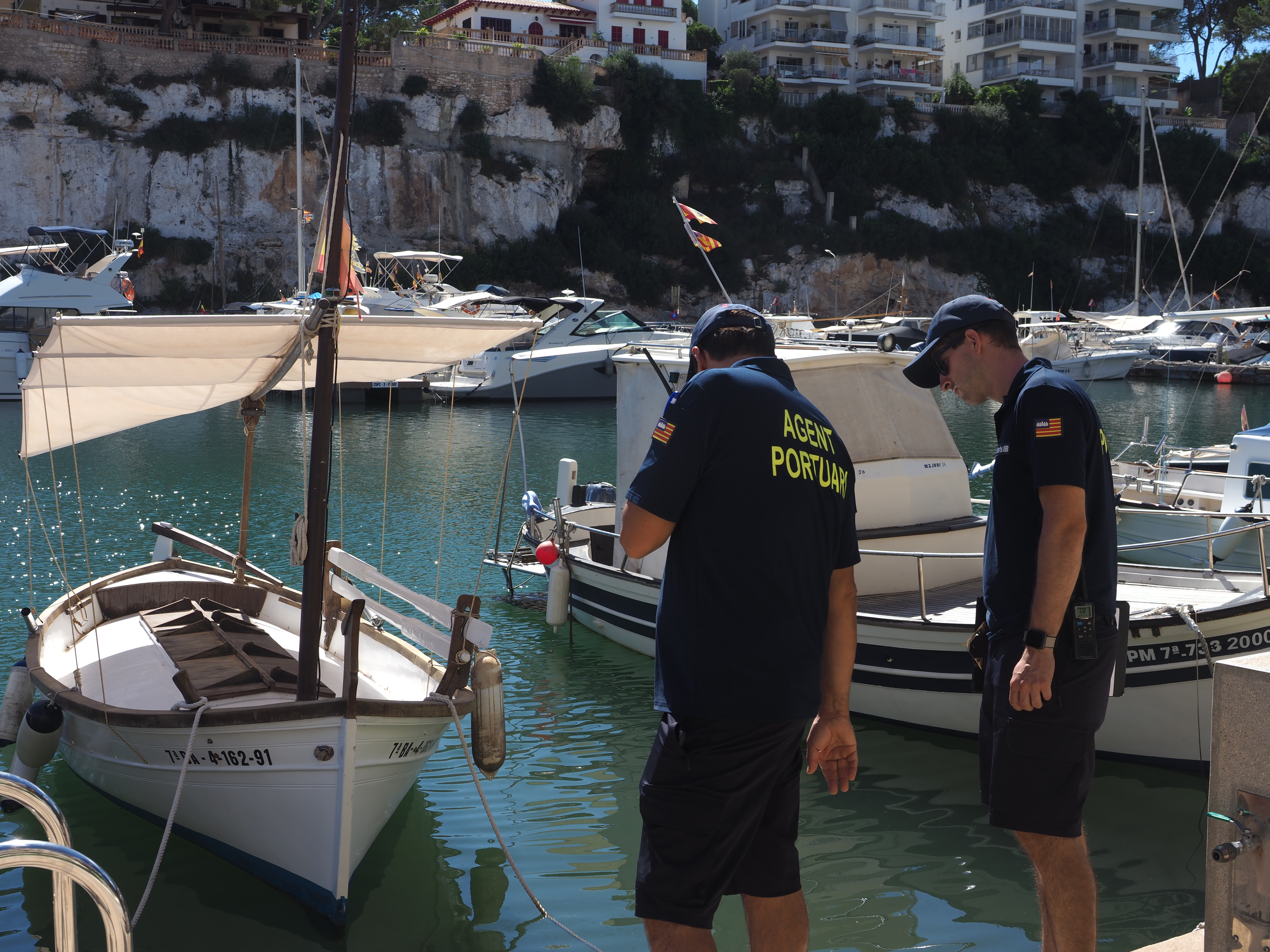 Dos agents portuaris miren els llaüts a un port de les Illes.