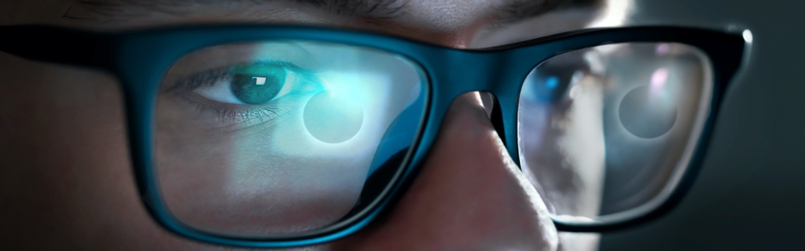 La pantalla de un ordenador con un eclipse solar se refleja en las gafas de un joven.