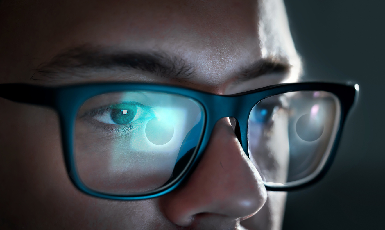 La pantalla de un ordenador con un eclipse de sol se refleja en las gafas de un joven.